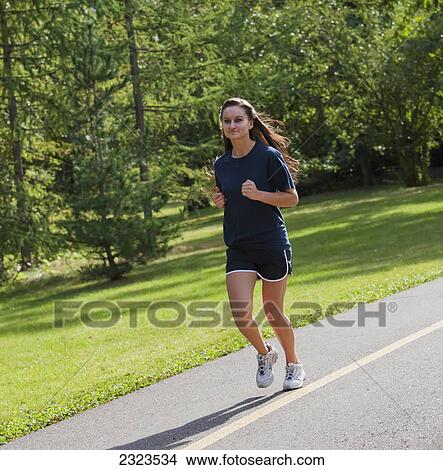 Picture - Young woman jogging on a pathway in a park; Edmonton alberta canada. Fotosearch