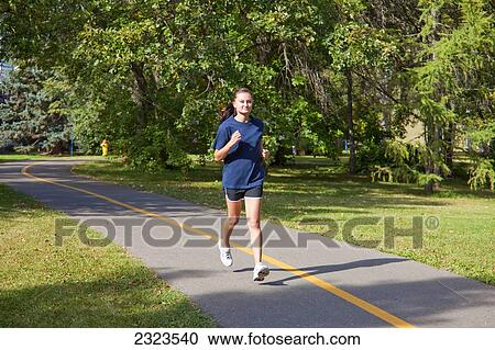 Stock Image - Young woman jogging on a pathway in a park; Edmonton alberta canada. Fotosearch