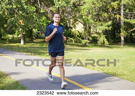 Stock Image - Young woman jogging on a pathway in a park; Edmonton alberta canada. Fotosearch