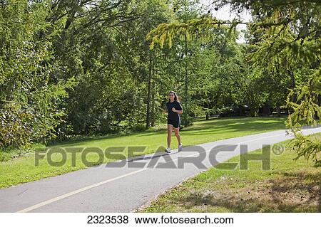 Stock Photo - Young woman jogging on a pathway in a park; Edmonton alberta canada. Fotosearch