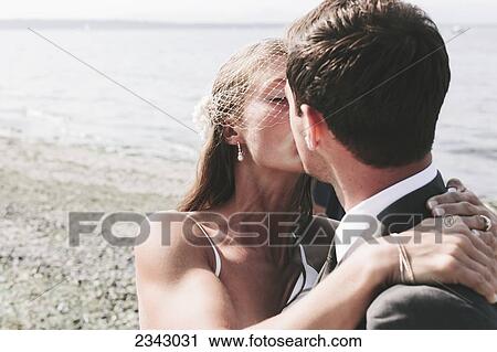 A bride and groom kissing on a beach at the water's edge; Kirkland, Washington, United States of America View Large Photo Image Stock Image - A bride and groom kissing on a beach at the water's edge; Kirkland, Washington, United States of America. Fotosearch