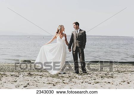 Stock Image - A bride and groom on a beach at the water's edge; Kirkland, Washington, United States of America. Fotosearch
