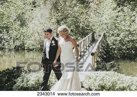 A bride and groom walk hand in hand with a bridge going over a creek; Pemberton, British Columbia, Canada View Large Photo Image Picture - A bride and groom walk hand in hand with a bridge going over a creek; Pemberton, British Columbia, Canada. Fotosearch