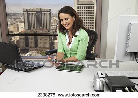 Stock Photography - A businesswoman sitting in her office with a view of buildings out the window; Portola Valley, California, United States of America. Fotosearch