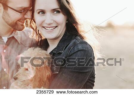 Stock Photo - A couple holding their pet dog; Crescent Beach, British Columbia, Canada. Fotosearch