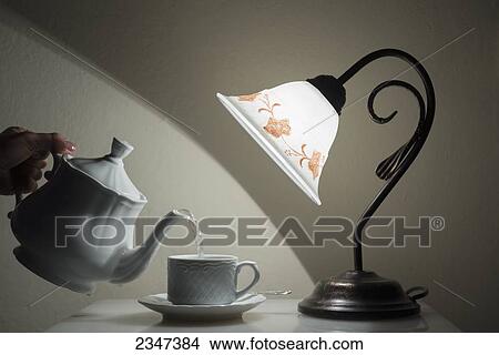 A lamp shining on a hand holding a teapot pouring tea into a teacup; Sestri Levante, Emilia-Romagna, Italy View Large Photo Image Picture - A lamp shining on a hand holding a teapot pouring tea into a teacup; Sestri Levante, Emilia-Romagna, Italy. Fotosearch