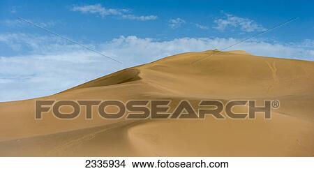 A large sand dune against a blue sky with cloud View Large Photo Image Picture - A large sand dune against a blue sky with cloud. Fotosearch