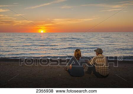 A man and woman sit on a beach watching the sunset on Lake Erie, Presque Isle State Park; Erie, Pennsylvania, United States of America View Large Photo Image Stock Photo - A man and woman sit on a beach watching the sunset on Lake Erie, Presque Isle State Park; Erie, Pennsylvania, United States of America. Fotosearch