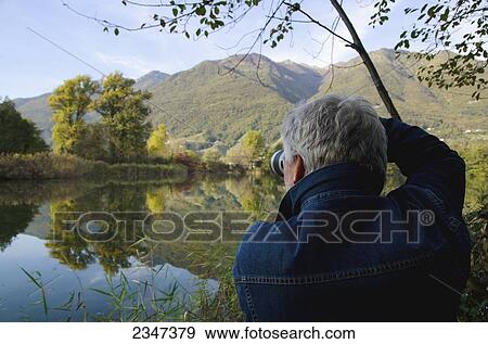 Stock Photo - A man photographs scenery across a tranquil lake; Locarno, Ticino, Switzerland. Fotosearch