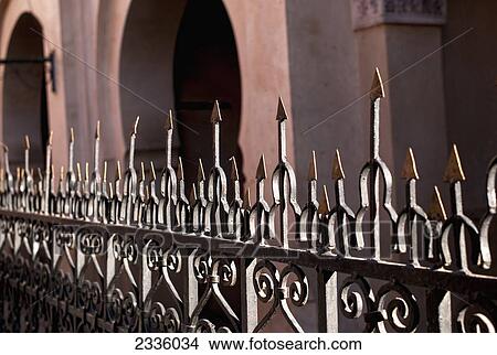 Picture - A metal railing with sharp pointed edges on top and a building with arched doorways. Fotosearch