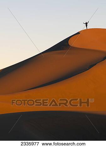 Stock Photo - A person stands on a top ridge of a sand slope. Fotosearch