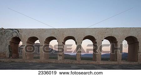 A structure with arches in a row and hills in the background at sunset View Large Photo Image Stock Photo - A structure with arches in a row and hills in the background at sunset. Fotosearch
