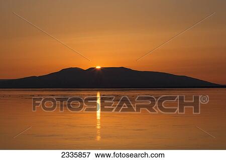 Stock Photo - A sunbeam reflected on the tranquil water at sunset with the sky and water glowing orange. Fotosearch