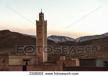Stock Image - A tower in the midst of buildings with mountains in the background at sunset. Fotosearch