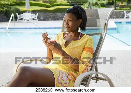 A woman eats a snack sitting in a lounge chair by the pool; California, United States of America View Large Photo Image Stock Image - A woman eats a snack sitting in a lounge chair by the pool; California, United States of America. Fotosearch