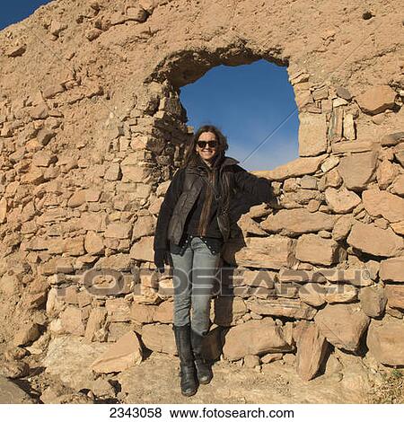 Stock Photo - A woman posing by a rock wall with a window; Ait Benhaddou, Sous-Massa-Draa, Morocco. Fotosearch