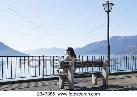A woman sitting on a bench overlooking Lake Maggiore; Brissago, Ticino, Switzerland View Large Photo Image Stock Photograph - A woman sitting on a bench overlooking Lake Maggiore; Brissago, Ticino, Switzerland. Fotosearch