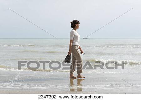A woman walking on the wet beach carrying her shoes; Rimini, Emilia-Romagna, Italy View Large Photo Image Stock Image - A woman walking on the wet beach carrying her shoes; Rimini, Emilia-Romagna, Italy. Fotosearch