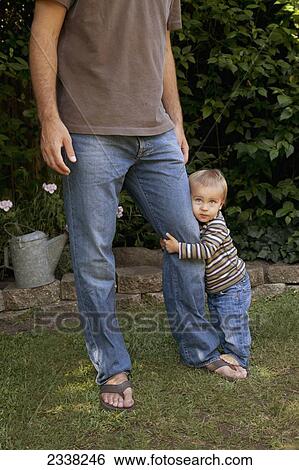 Stock Photograph - A young boys holds onto his father's leg; Pacifica, California, United States of America. Fotosearch