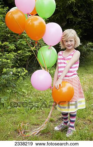 Stock Photo - A young girl standing on the grass with a colourful bouquet of balloons; Pacifica, California, United States of America. Fotosearch