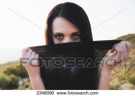 A young woman outside, covering a part of her face behind a black piece of sheen fabric; California, United States of America View Large Photo Image Stock Image - A young woman outside, covering a part of her face behind a black piece of sheen fabric; California, United States of America. Fotosearch