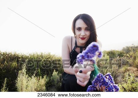 A young woman presenting a purple flower to the viewer; California, United States of America View Large Photo Image Picture - A young woman presenting a purple flower to the viewer; California, United States of America. Fotosearch
