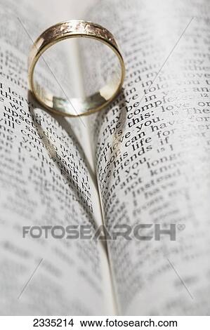 Picture - Close up of a gold ring with the shadow of an heart on book about love; Calgary, Alberta, Canada. Fotosearch