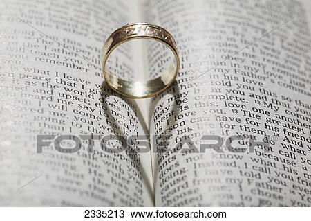 Stock Image - Close up of a gold ring with the shadow of an heart on book about love; Calgary, Alberta, Canada. Fotosearch