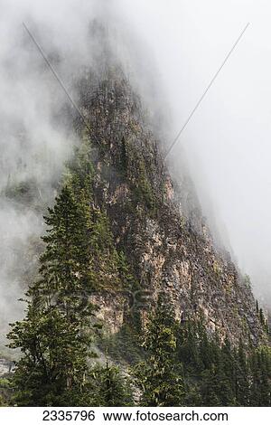 Stock Photograph - Clouds covering the steep cliff on the side of a mountain. Fotosearch