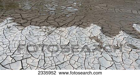 Stock Image - Dry cracked ground with water soaking into it. Fotosearch
