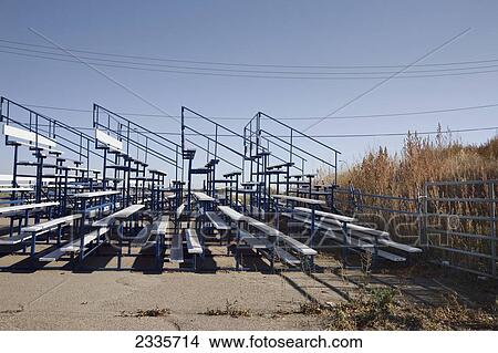 Empty outdoor stadium bleachers against a fence overlooking a field of tall grasses: Lethbridge, Alberta, Canada View Large Photo Image Picture - Empty outdoor stadium bleachers against a fence overlooking a field of tall grasses: Lethbridge, Alberta, Canada. Fotosearch