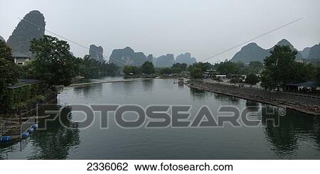 Houses along the water's edge with rugged mountain peaks in the background View Large Photo Image Stock Image - Houses along the water's edge with rugged mountain peaks in the background. Fotosearch