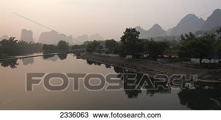 Houses along the water's edge with rugged mountain peaks in the background View Large Photo Image Stock Image - Houses along the water's edge with rugged mountain peaks in the background. Fotosearch