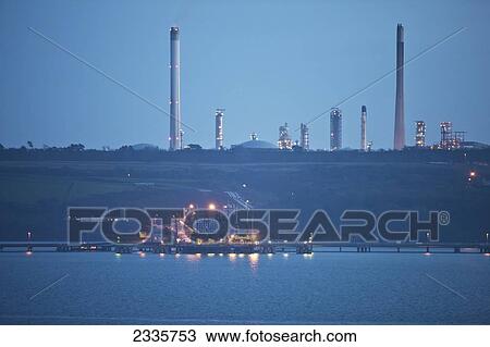 Lights illuminate a structure on a pier over the water with smoke stacks in the background View Large Photo Image Stock Image - Lights illuminate a structure on a pier over the water with smoke stacks in the background. Fotosearch