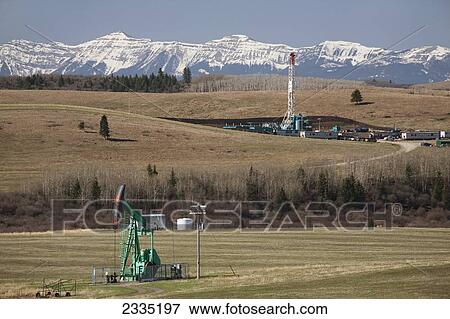Pumpjack and rig in rolling hills with snow covered mountains and blue sky in the background; Longview, Alberta, Canada View Large Photo Image Stock Photo - Pumpjack and rig in rolling hills with snow covered mountains and blue sky in the background; Longview, Alberta, Canada. Fotosearch
