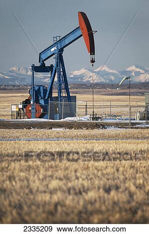 Pumpjack in a field with snow covered mountains and blue sky at sunrise; Alberta, Canada View Large Photo Image Stock Photo - Pumpjack in a field with snow covered mountains and blue sky at sunrise; Alberta, Canada. Fotosearch