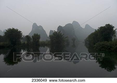 Rock formations and trees in a haze and reflected in tranquil water View Large Photo Image Stock Photo - Rock formations and trees in a haze and reflected in tranquil water . Fotosearch