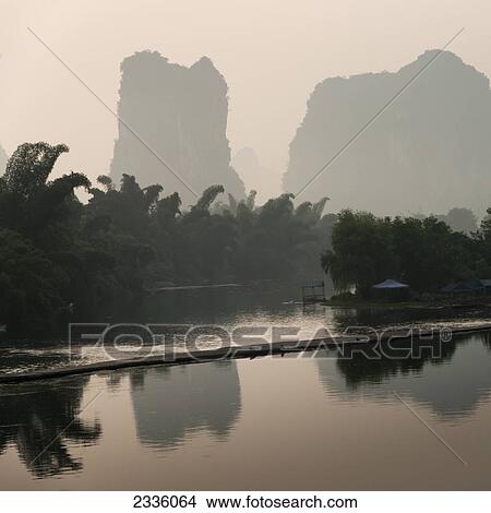Rugged mountain peaks and trees reflected in a tranquil river at sunset View Large Photo Image Picture - Rugged mountain peaks and trees reflected in a tranquil river at sunset. Fotosearch