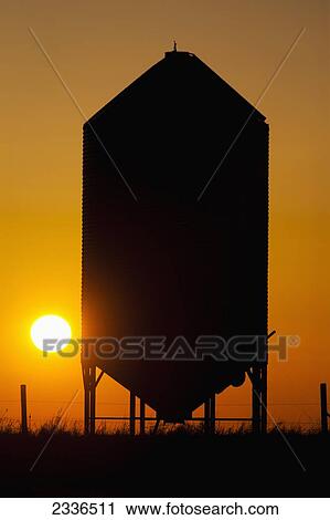 Stock Image - Silhouette of a grain bin with orange sun; Alberta, Canada. Fotosearch