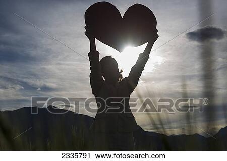 Silhouette of a woman holding up a large heart shape against the sunlight View Large Photo Image Stock Image - Silhouette of a woman holding up a large heart shape against the sunlight. Fotosearch