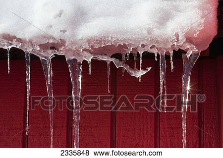 Stock Photo - Snow and icicles against a red wall and melting in the sunlight. Fotosearch