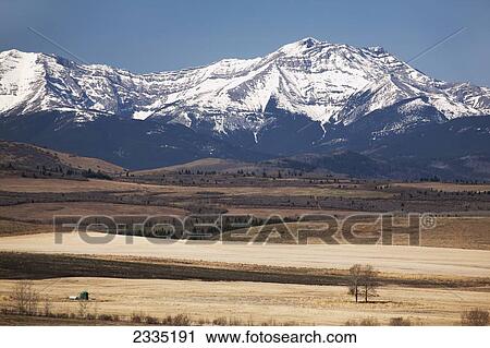 Stock Image - Snow covered mountain range with foothills in the foreground and blue sky; Longview, Alberta, Canada. Fotosearch