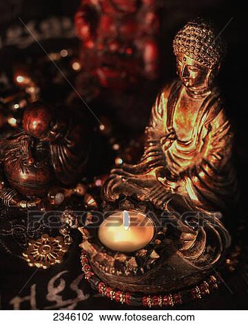 Stock Image - Statues of Buddha illuminated by a single white candle in a dark environment; California, United States of America. Fotosearch