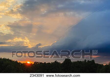 Sun setting over the trees with storm clouds in the sky; Ohio, United States of America View Large Photo Image Stock Image - Sun setting over the trees with storm clouds in the sky; Ohio, United States of America. Fotosearch