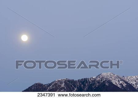Stock Image - The sun shining brightly in a blue sky over the swiss alps; Locarno, Ticino, Switzerland. Fotosearch