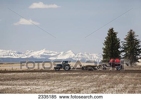 Tractor with air seeder planting crop in field with snow covered mountains and blue sky and clouds; Alberta, Canada View Large Photo Image Stock Photography - Tractor with air seeder planting crop in field with snow covered mountains and blue sky and clouds; Alberta, Canada. Fotosearch