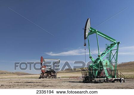 Picture - Two pumpjacks in a field with blue sky and clouds; Longview, Alberta, Canada. Fotosearch