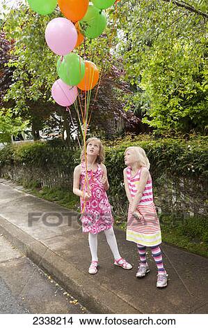 Two young girls standing on a sidewalk with a bouquet of balloons; Pacifica, California, United States of America View Large Photo Image Picture - Two young girls standing on a sidewalk with a bouquet of balloons; Pacifica, California, United States of America. Fotosearch