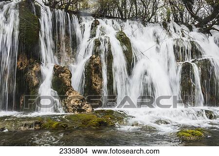 Picture - Waterfalls over rugged cliffs of rock and trees up above. Fotosearch