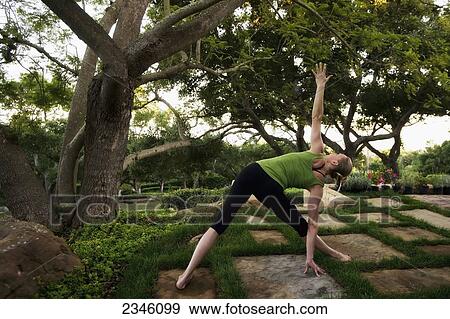Stock Photo - Woman in a yoga pose stretching on tiles by a tree; California, United States of America. Fotosearch